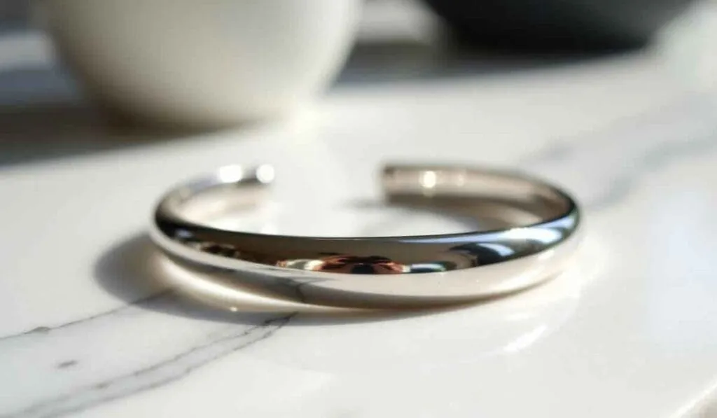 A shiny silver metal bracelet lying open on a white marble surface.